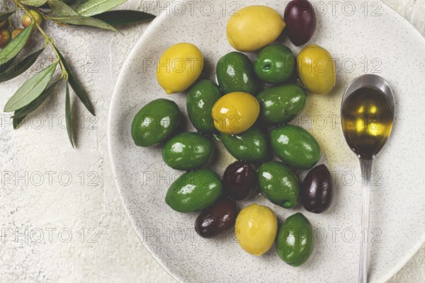 A mix of olives, a variety of Chalkidiki, verdi giganti and Kalamata, on a plate with a spoonful of olive oil, top view, no people