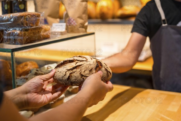 Customer hands in the bakery shop buying a loaf from the baker in the workshop workshop
