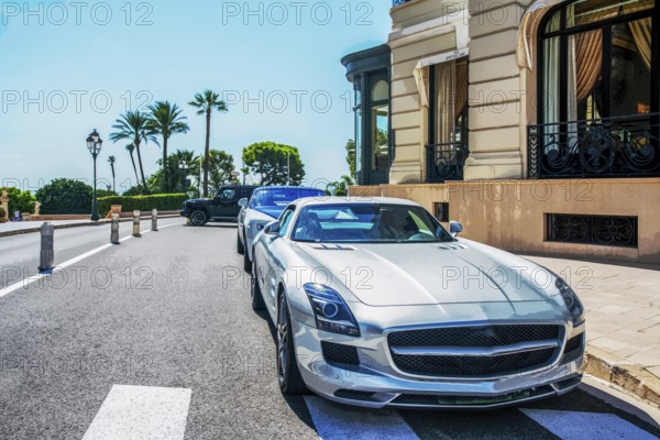 Luxury cars at parking lot in 5 meters from old building of casino Monte Carlo, behind palm trees in Monaco Royalty, fantastic summer recreation there and at French Riviera in summer