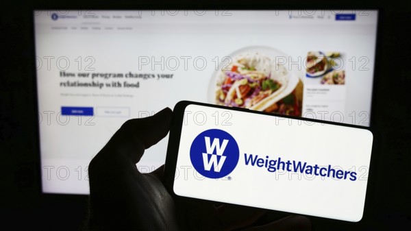 Stuttgart, Germany, 03-19-2023: Person holding cellphone with logo of WW International Inc. (Weight Watchers) on screen in front of business webpage. Focus on phone display, Europe