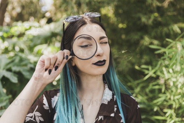 Young woman holding magnifying glass one eye