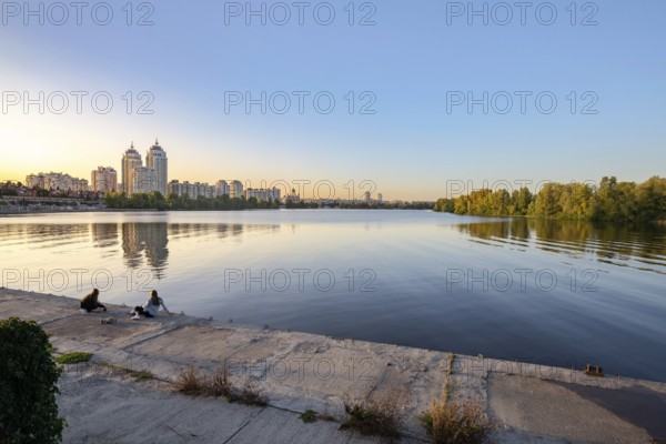 Ukraine, September 22, 2020, Two girls on the embankment close to the high Obolon buildings near the Dnieper river in Kiev, Ukraine. Blue clear sky and reflection in the water, Europe
