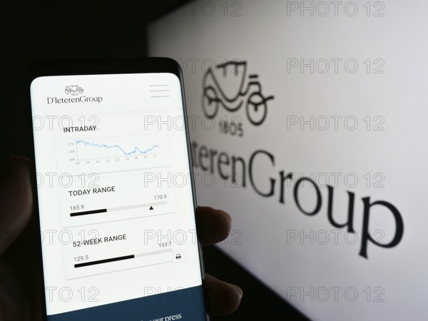 Stuttgart, Germany, 03-18-2023: Person holding cellphone with web page of Belgian automotive company D'Ieteren S.A. on screen in front of logo. Focus on center of phone display, Europe