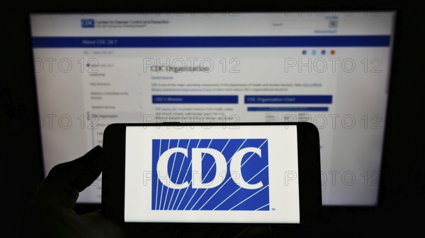 Stuttgart, Germany, 01-15-2022: Person holding cellphone with logo of US Centers for Disease Control and Prevention (CDC) on screen in front of webpage. Focus on phone display, Europe
