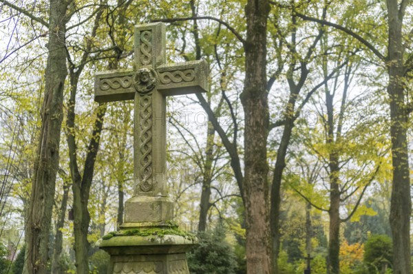 Old weathered celtic cross tombstone standing in a peaceful cemetery during fall
