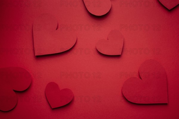 Red hearts cut from paper on red background, paper craft origami style, from above. Romantic Valentines day red monochrome background, love concept. Different size hearts top view, paper art design