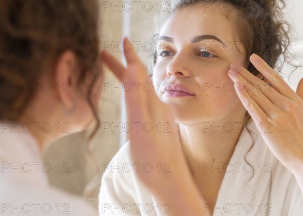 Woman applying cream face while looking mirror 2