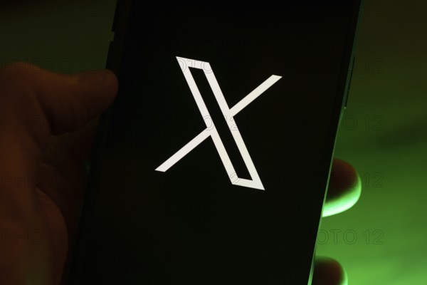 Hand holding a smartphone with the X application logo