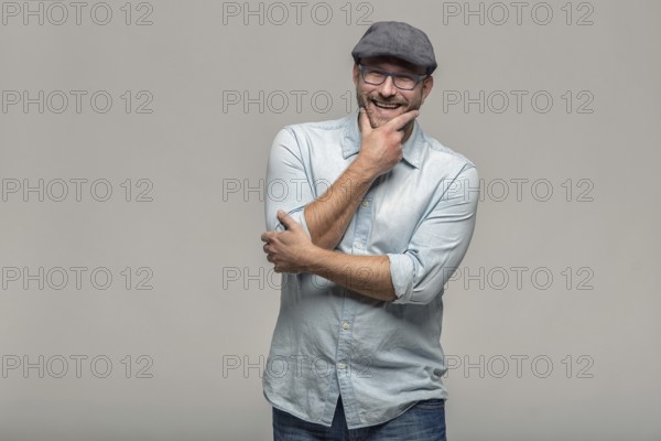 Thoughtful attractive middle-aged man with his finger to his mouth standing looking towards the camera on a grey background