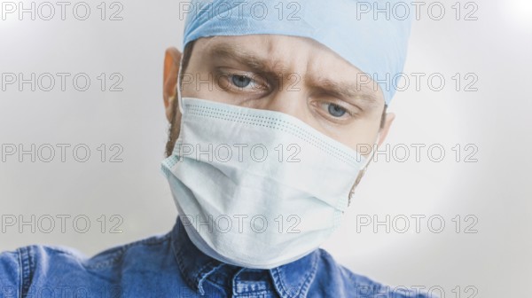 A focused medical professional wearing a mask and surgical cap, looking down