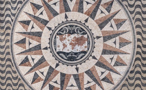 Aerial view of pavement map with routes of Portuguese explorations by Monument to Discoveries, Belem, Lisbon, Portugal, Europe. Antique map maritime motifs, compass, wind rose, image decorations, calcada patterns made of pale, black and red limestone, Europe