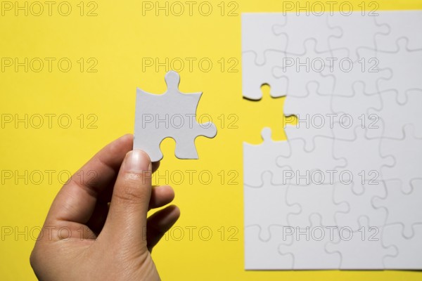 Person s hand holding missing white jigsaw puzzle piece yellow backdrop