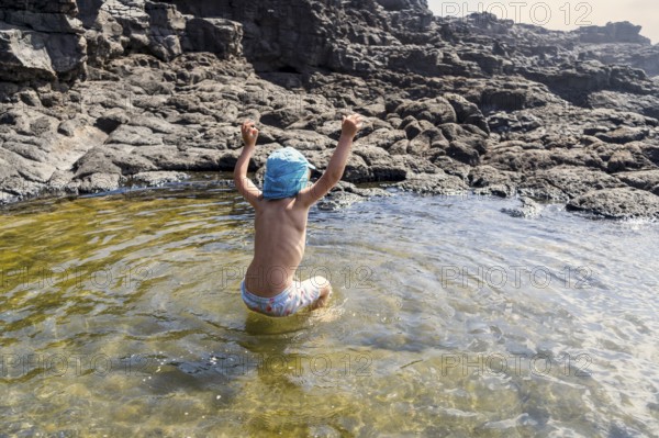 Small boy cheerfully jumping in Charcones natural pools in Lanzarote, Canary Islands, Spain, Europe