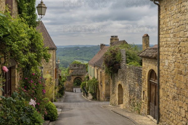 Domme, France - 12 May, 2022: picturesque street with stone houses and blossoming flowers in the historic village of Domme in the Dordogne Valley
