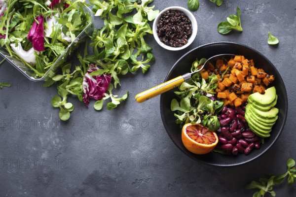 Quinoa salad in bowl with avocado, sweet potato, beans, herbs, orange on concrete rustic background. Quinoa superfood concept. Clean healthy detox eating. Veganvegetarian food. Making healthy salad