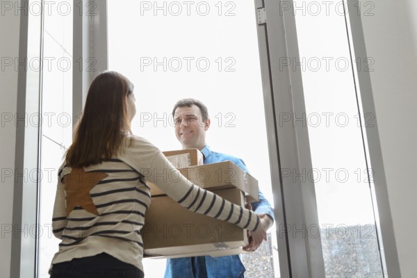 Fast and reliable service. Cheerful young courier giving a cardboard box to a young woman standing at the entrance to her apartment