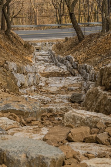 Drainage ditch constructed of large boulders on side of mountain on early spring afternoon in South Korea