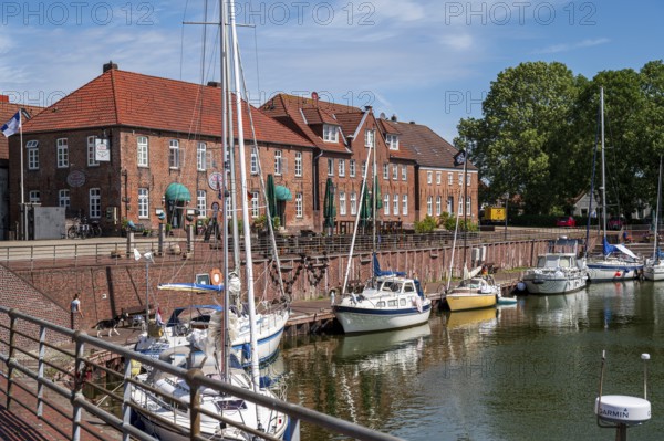 Sailing yachts on the promenade with brick houses and a terrace in sunny weather and blue sky, Hooksiel, Wangerland, Lower Saxony