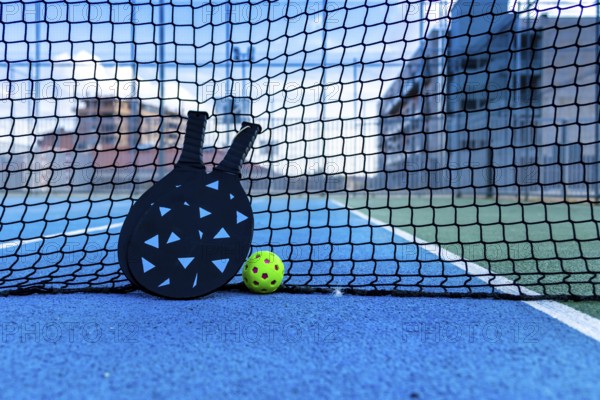 Pickleball ball and paddles resting on the net of a pickleball court
