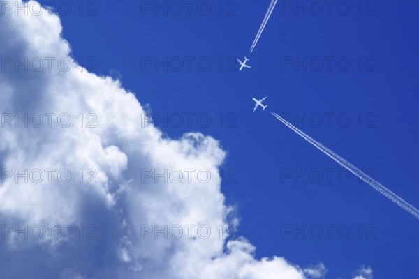 Two passenger airplanes with contrails on a collision course in the blue sky with clouds