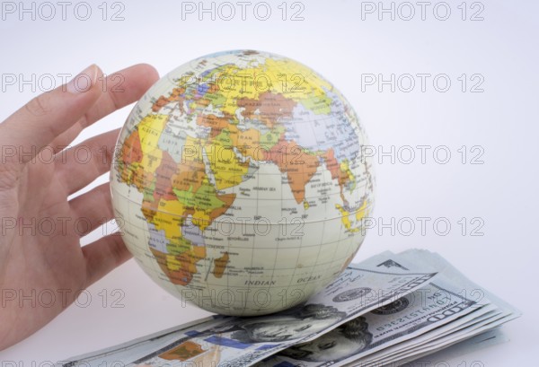 Human hand holding a model globe by the side of aAmerican dollar banknotes on white background