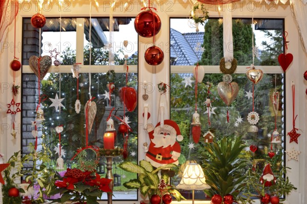 Christmas decorated window with fairy lights, Christmas balls, hearts, stars, bells, candle, Santa Claus and plants on the windowsill