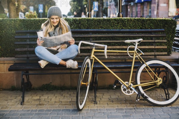 Pretty woman reading newspaper near bicycle