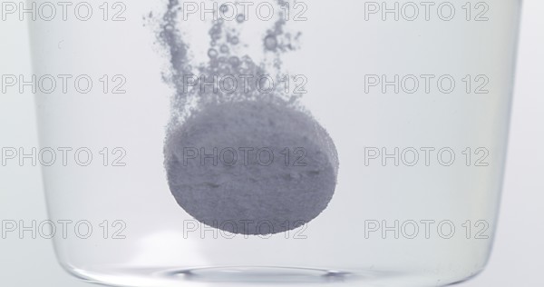 Tablets Falling and Dissolving into a Glass of Water against White Background