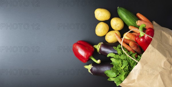 above view of fresh organic vegetables spilling out of paper shopping bag on dark kitchen counter, healthy eating and cooking concept