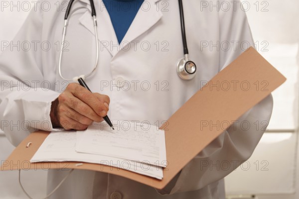 Unrecognizable doctor in white coat and stethoscope writing a prescription for a patient in his folder