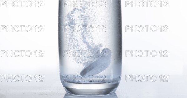 Tablets Falling and Dissolving into a Glass of Water against White Background