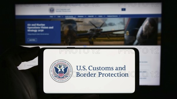 Stuttgart, Germany, 10-29-2023: Person holding mobile phone with seal of agency United States Customs and Border Protection (CBP) in front of web page. Focus on phone display, Europe