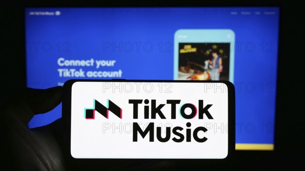 Stuttgart, Germany, 07-30-2023: Person holding cellphone with logo of streaming service TikTok Music on screen in front of company webpage. Focus on phone display, Europe