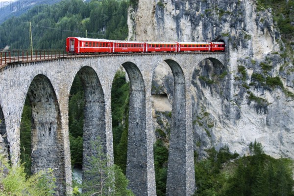 Red train of swiss Rhätische Bahn, Rhaetian Railway Company or Glacier Express on Viaduct Landwasserviadukt, near town of Filisur, Grisons, Switzerland, Europe