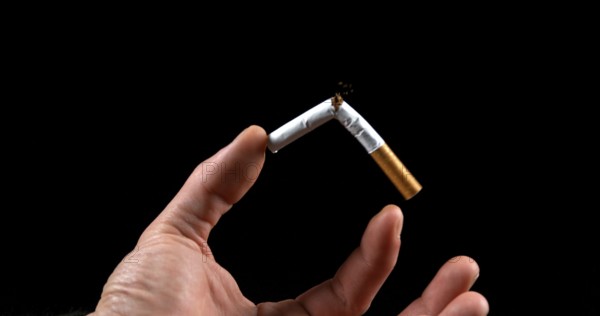 Hand of Man who breaks a Cigarette on Black Background