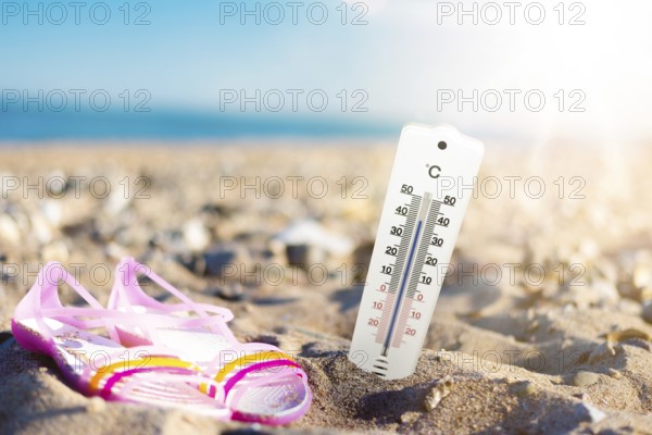 summer weather and hear concept, thermometer in sand at beach against sea and blue sky