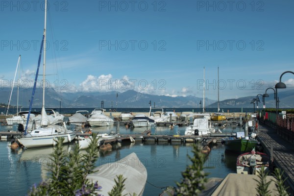 A harbour with numerous boats, mountains in the background and a clear sky, Sirmione, Lake Garda, Italy, Europe