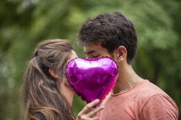 Couple kissing, covered by heart-shaped balloon