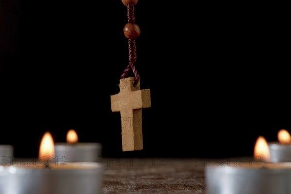 Circle of lighted candles with a wooden Rosary praying beads in the center and a smoldering incense in the background isolated on a black background