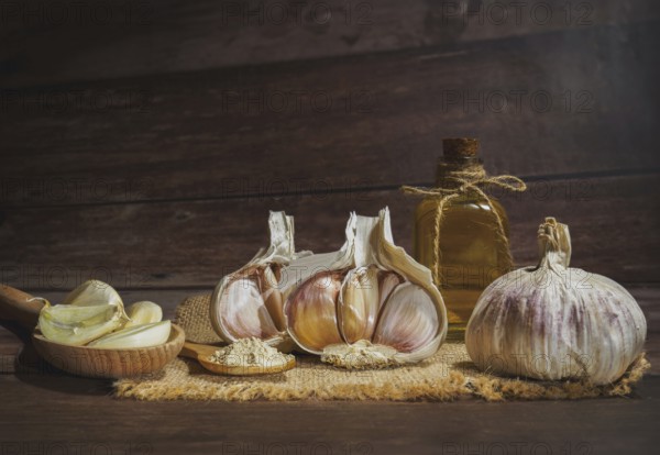 Whole, powdered and chopped garlic on a burlap cloth with a glass bottle with olive oil on a wooden table
