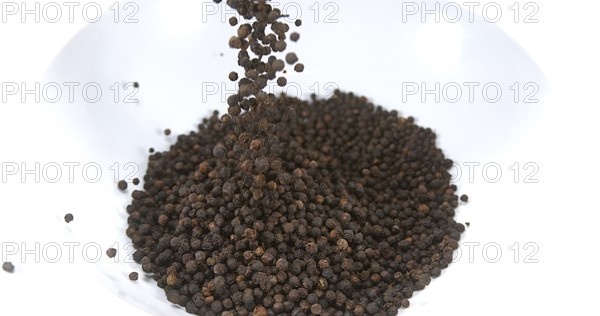 Black Peppercorns falling against White Background