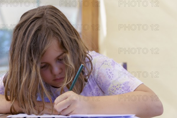 Close-up of a beautiful blonde girl in a colorful dress concentrating on school homework