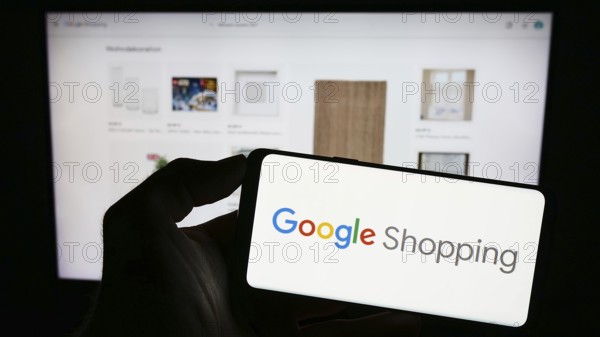 Stuttgart, Germany, 09-23-2023: Person holding mobile phone with logo of product search platform Google Shopping on screen in front of company web page. Focus on phone display, Europe