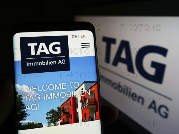 Stuttgart, Germany, 05-21-2022: Person holding smartphone with website of German real estate company TAG Immobilien AG on screen with logo. Focus on center of phone display, Europe