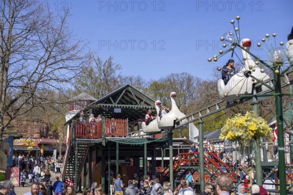 Copenhagen, Denmark, April 21, 2019: Amusement park ride and crowd of people at Bakken, the oldest amusement park in the world, Europe