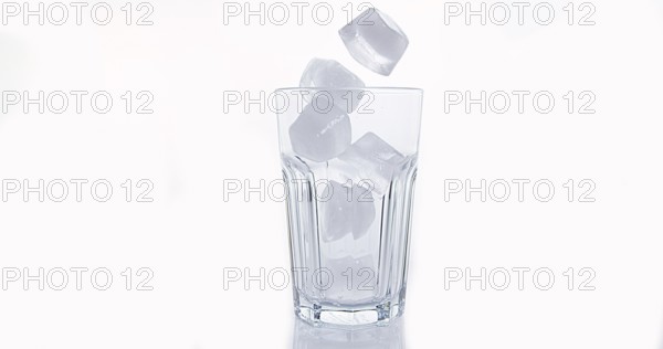 Ice Cubes Falling into Glass against White Background