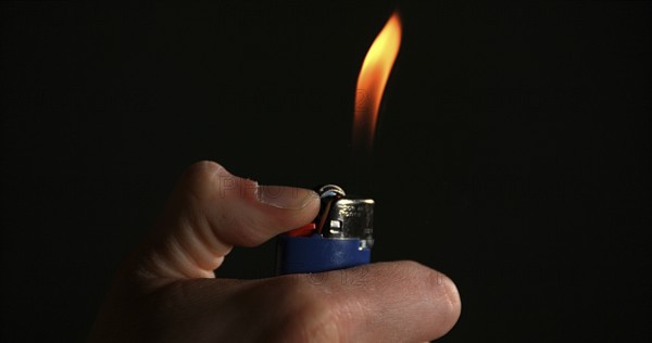 Lighter in Hand with Flame against Black background