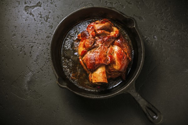 Traditional German cuisine - Roasted pork knuckle eisbein (Schweinshaxe) in iron pan on black background