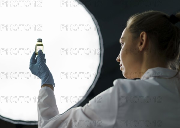 Female researcher laboratory holding vaccine bottle light