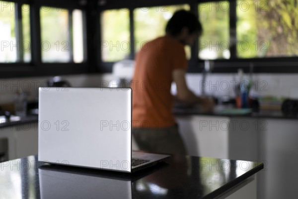 Laptop on the kitchen island. Man washing the dishes and doing remote work from his kitchen